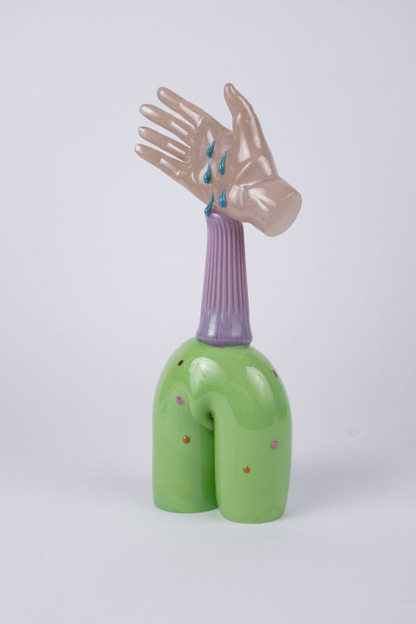 Rasmus Nossbring glasskulptur, beige hand med blå rinnande tårar. Lila pelare ovanpå en grön båge med röda prickar.