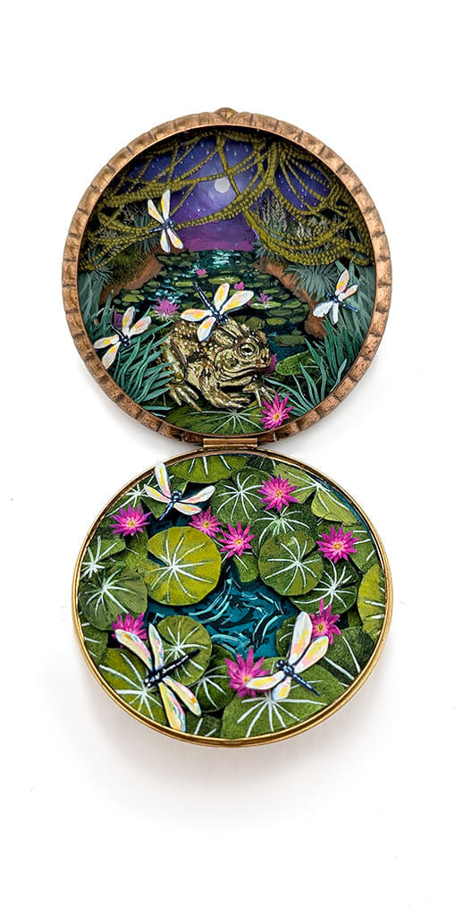 hand-cut watercolor collage in antique cosmetic compact by Shannon Taylor of several dragonflies flying over a pond with a large frog and lily pads