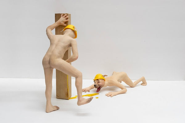 sculpture of two anthropomorphic dogs with constructions hats, one standing and peeing and the other down on the ground licking the pee