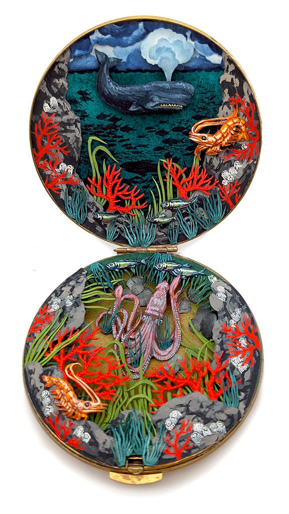 hand-cut watercolor collage in antique cosmetic compact by Shannon Taylor of an underwater scene on the bottom with a squid and coral reef and on the top is a blue whale out of the water.