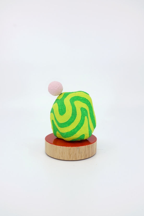 Green and yellow painted sculpture with a small light pink sphere on top of it