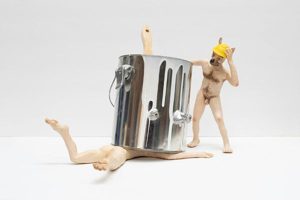 sculpture of nude anthropomorphic dog crushed under a silver paint can and another dog watching