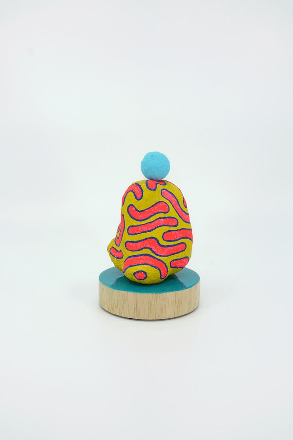 Yellow shaped sculpture with pink squiggles and a blue sphere on it