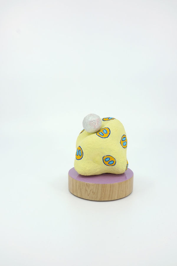 Yellow blob shaped sculpture on a pink circular wooden stand