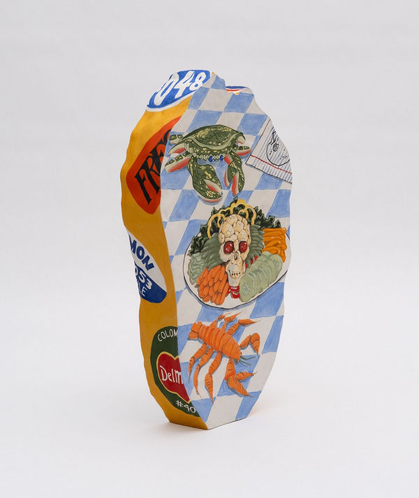 Flat sculpture of a cabbage with a painting of a table with a plate of vegetables, a crab and a lobster on a blue and white checkered table clothe. On the side of the sculpture is yellow with fruit and vegetable stickers. On the back is a realistic painting of a green cabbage