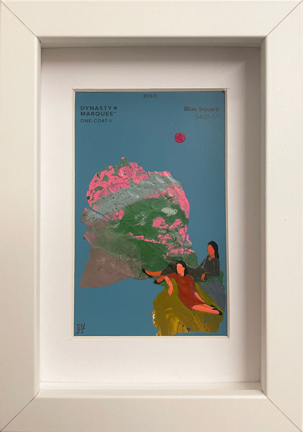 Painting on a blue paint chip of two women in dresses sitting on a green hill in white frame