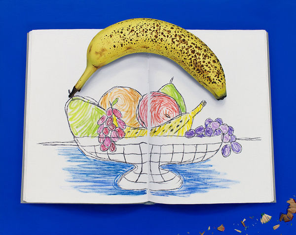 hyper realistic painting by artist Sara Suppan depicting a sketchbook with a rudimentary sketch of a fruit bowl with a spotted banana holding the pages open against a deep blue background with pencil shavings beside it