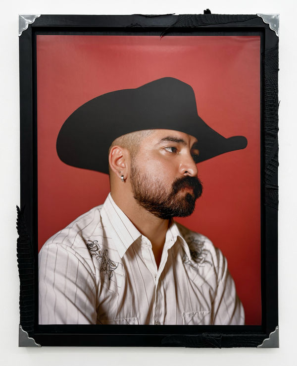 Photo of a man with a beard wearing a black cowboy hat and a white shirt on a red background