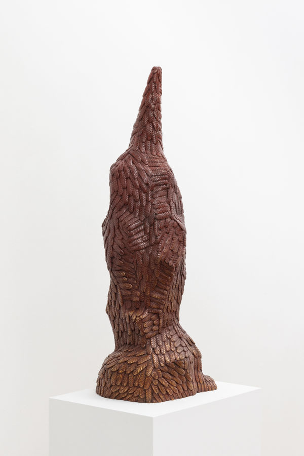 Free-standing bronze sculpture of a form resembling a penguin whose beak is directed upward. The sculpture is cast entirely in feathers and treated with a maroon and gold patina.