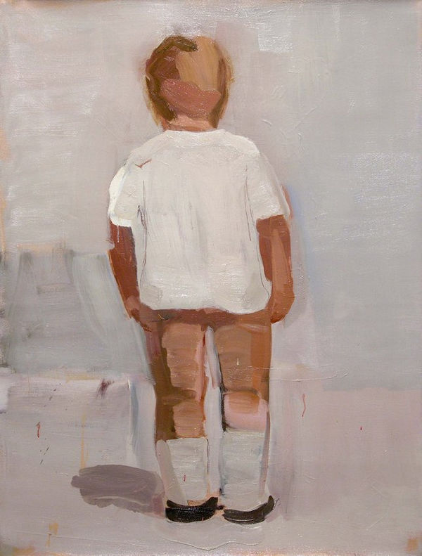 Small child with his back to the viewer wears white t-shirt and tan pants in front of plain gray background.
