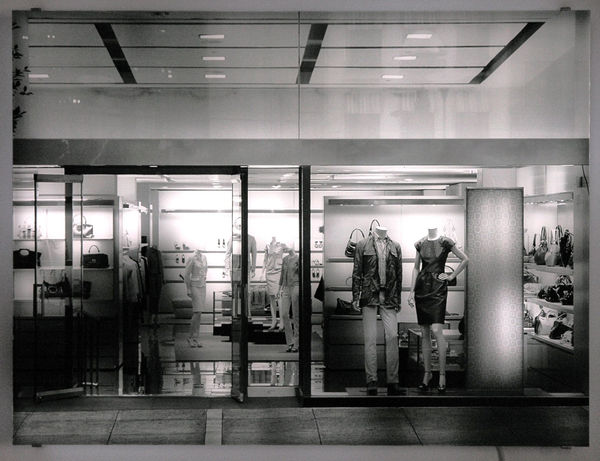 Still image of rectangular piece with white LEDs behind photographic image of a store front mounted on Plexiglass The LEDs display shadowy images of people walking back and forth in front of into and out of the store