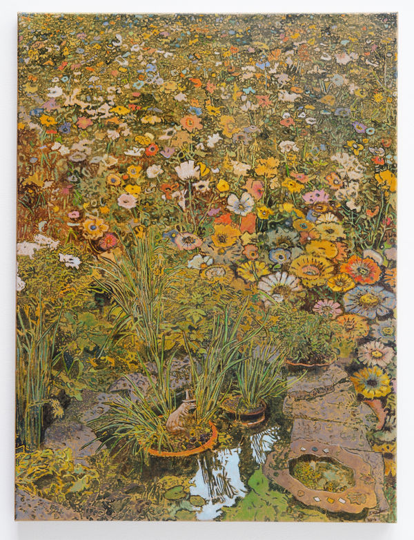Tiny man-made pond with small frog sculpture and lilypads is surrounded by stones and dense thicket of multi-colored flowers.