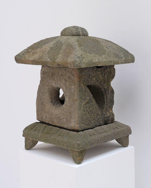Weathered stone lantern with square base and feet, square body with hole in the center, and domed topper.