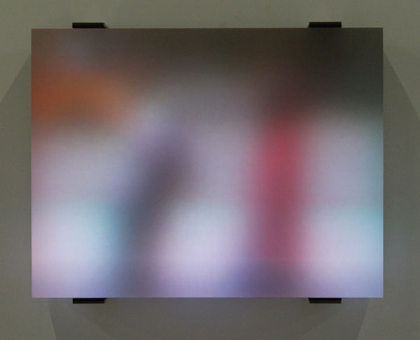 Still image of multiple multi-colored LEDs blurred behind thick block of resin show people walking along a sidewalk