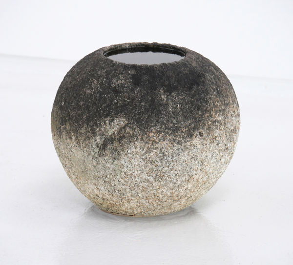 Rounded stoned basin with dark weathering towards the top of the bowl that holds water.