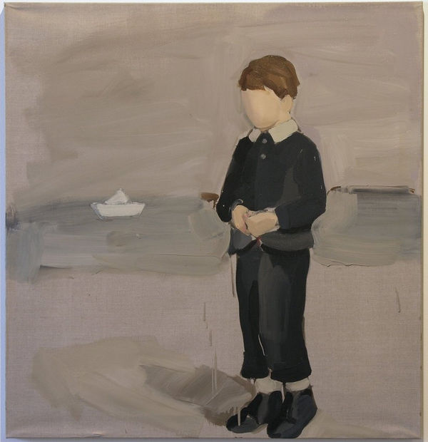 Young faceless boy in navy outfit stands in front of the water with a sailboat to his right.