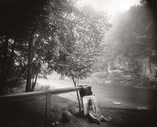 Virginia sleeping on patio with alligator swim toy on river's edge in background, from the Immediate Family series by Sally Mann