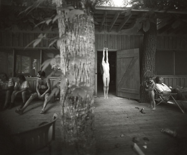 Jessie Mann nude hanging on a hayhook with Larry Mann and Virginia Mann and tree in foreground, from the Immediate Family series by Sally Mann
