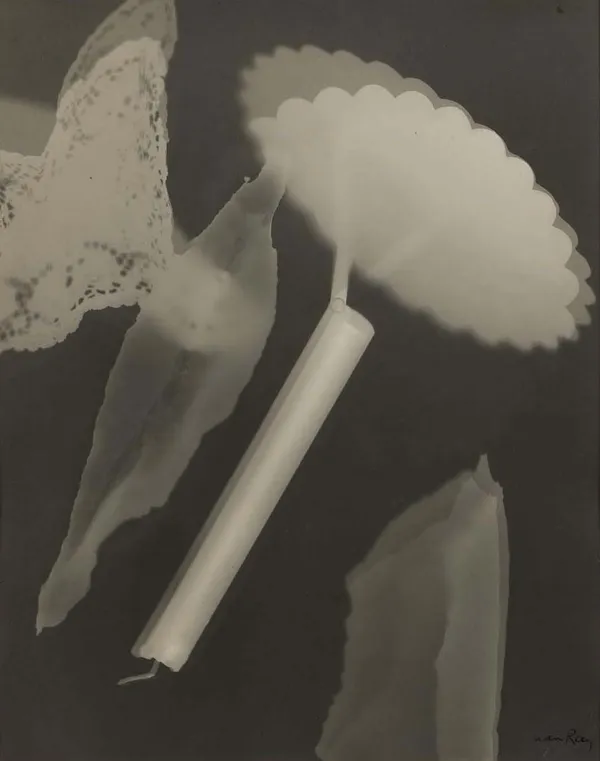 Man Ray Rayograph featuring abstract shapes, lace, and a scalloped object arranged in surreal composition on photographic paper without a camera.