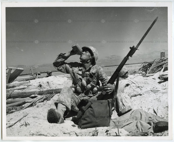 "Time Out" Marine draped with hand grenades and extra clip of ammunition takes time out for a drink from his canteen on Tarawa., 1943