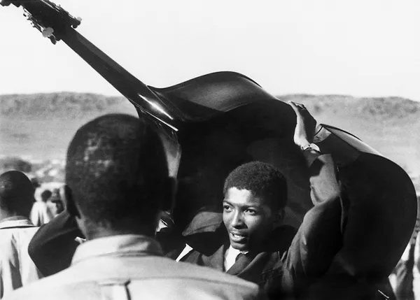 Alf Kumalo, A committed young musician carrying his double bass through a crowd, Soweto, c.1960s