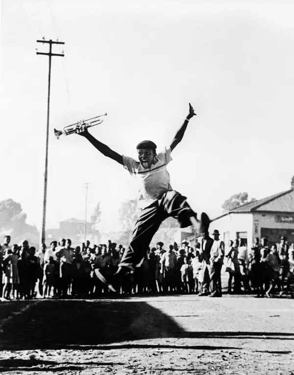 Alf Kumalo, Hugh Masekela leaps into the air with delight after receiving a trumpet from American jazz legend, Louis Armstrong, 1956