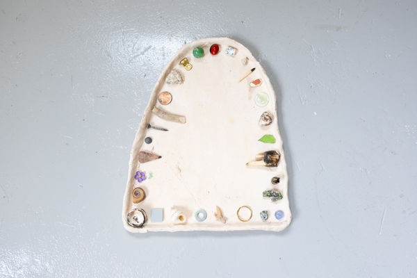 An arched ceramic dish by Jon Gott with small found materials organized in an orderly fashion around the outer edge.