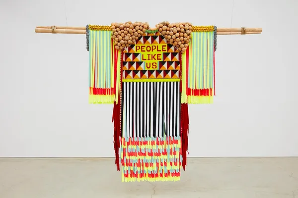 Jeffrey Gibson PEOPLE LIKE US, 2019 Canvas, cotton, linen, brass grommets, nylon thread, cotton thread, artificial sinew, glass and plastic beads, nylon fringe, grosgrain ribbon, tin jingles, wooden tipi poles, deer hide Garment: 85 x 68 x 8 in (215.9 x 172.7 x 20.3 cm), Tipi pole: 4 x 4 x 120 inches (10.2 x 10.2 x 304.8 cm)