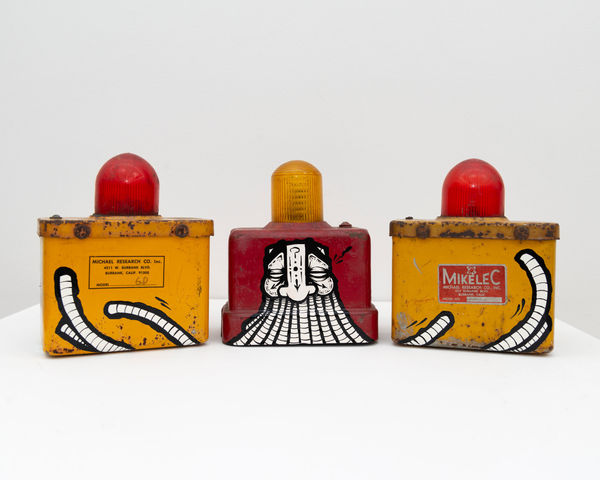 Two yellow with red light on top and a red with yellow light on top antique emergency road lights with GATS character painted across the three lights in black and white