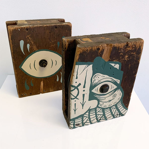 Two wood blocks with imagery in a teal blue, white, and off-white color painted overtop.