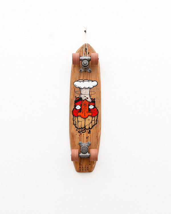 Brown wooden vintage skateboard with a red face GATS character with an atomic bomb smoke ring coming out of the top of his head painted on the bottom of the board