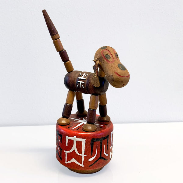 Small wood sculpture of a dog, painted with little red and white symbols/designs.