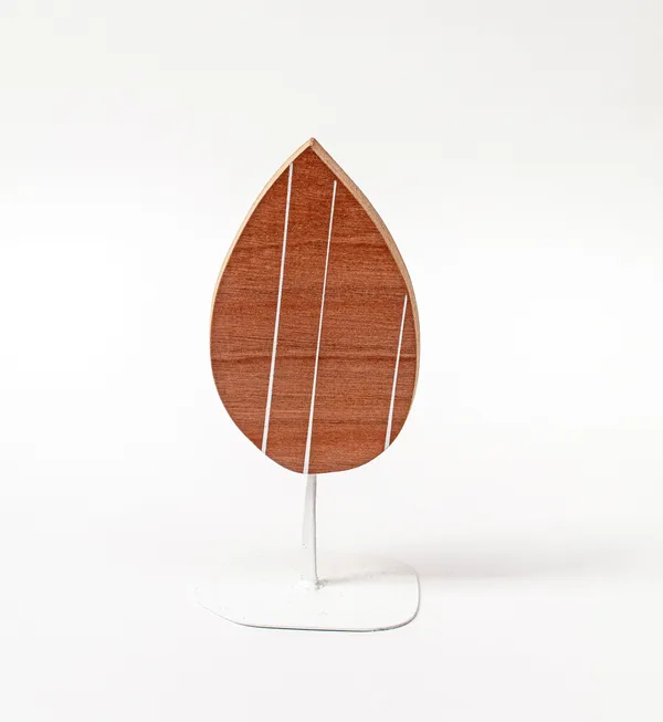 Wooden sculpture of a tear drop shaped piece of wood with three white stripes vertically across it on a white steal stand