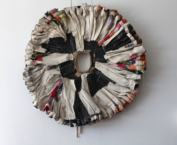 Circular sculpture with small hole in the center comprised from canvas, fabric, gesso, graphite, hardware, thread, spray paint, and wood