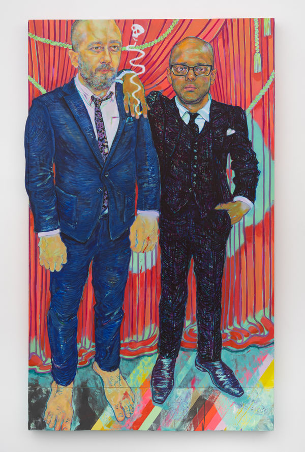 Two men in suits one barefoot the other shod in front of red stage curtain