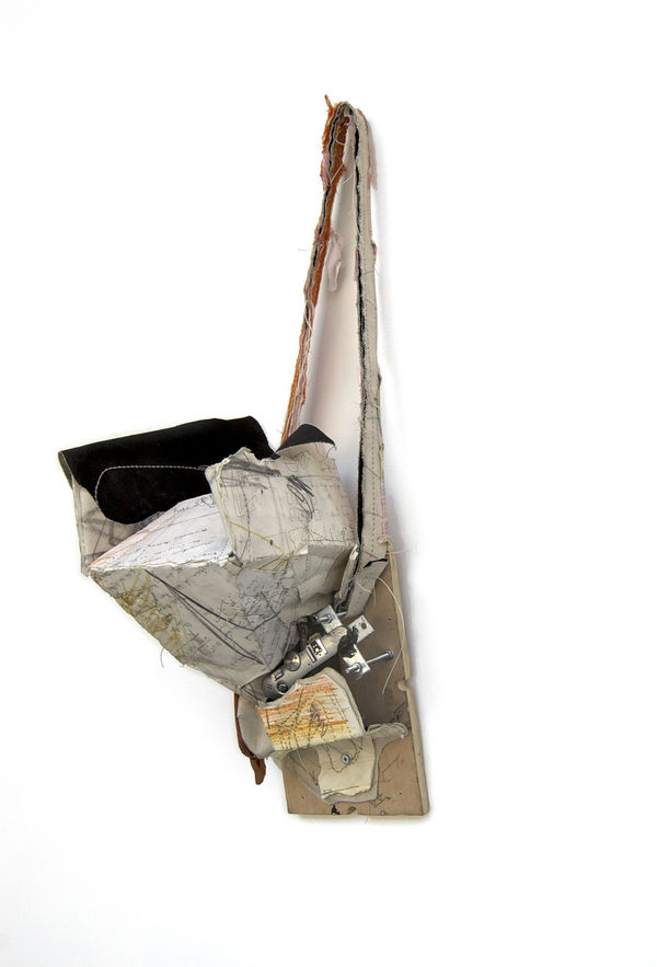 Sculpture containing digital camera parts hangs from a strap on the wall