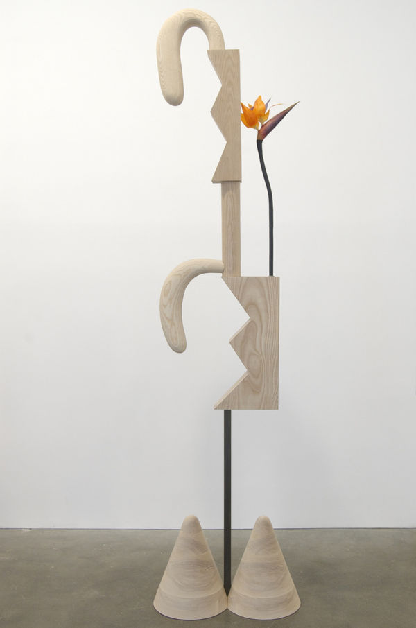 Carved wood abstraction in blonde wood, two cones as base attached to rod and wood carving with two long rabbit ear shapes, orange flower inserted into structure