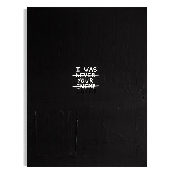 A vertical black and white typographic painting featuring the hand-painted text "I WAS NEVER YOUR ENEMY" with "NEVER" struck through, and the word "LOVER" emphasized at the bottom against a dark, textured background.