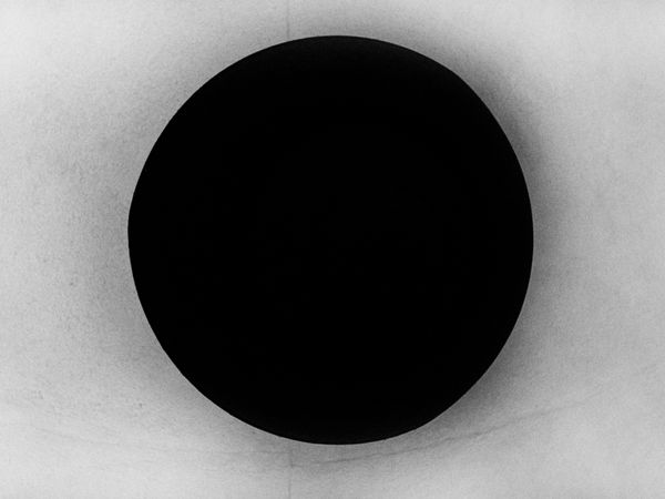 A minimalist black and white composition titled "The Passage," featuring a large, solid black circle centered against a textured, light-colored background with a soft horizontal horizon line.