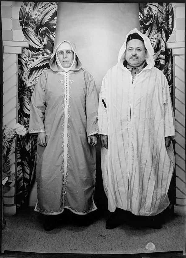 1960s black and white photograph of a man and a woman standing wearing a hooded algerian dress