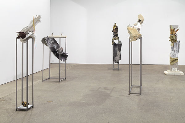 Installation view of Matthew Monahan's sixth solo show at Anton Kern Gallery, featuring sixteen sculptures, a set of drawings, two wall-mounted masks, and a single large figure in the back room. A few sculptures.