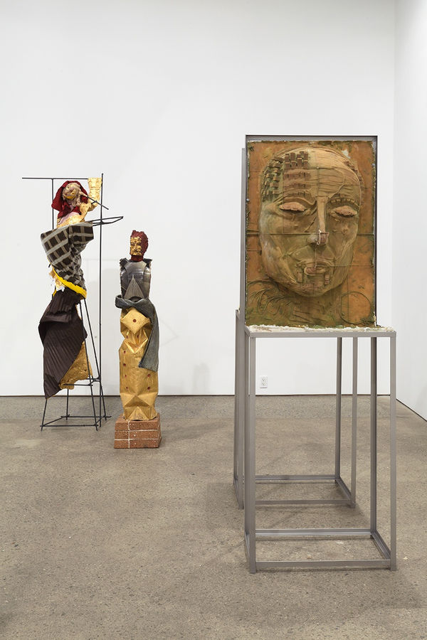 Installation view of Matthew Monahan's sixth solo show at Anton Kern Gallery, featuring sixteen sculptures, a set of drawings, two wall-mounted masks, and a single large figure in the back room. Three works.