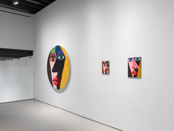 installation view of Brian Calvin's Waiting featuring paintings with hyperbolic color, mosaic eyes, and more. Two small rectangular works next to one of Calvin's circle canvases.