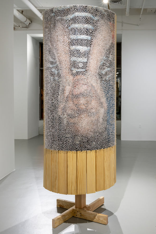 Round freestanding wood sculpture with two images of human figures adhered to the surface and obscured by thousands of clear push pins