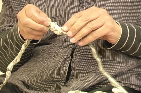 Still image of Maren Hassinger's hands twisting newspaper 