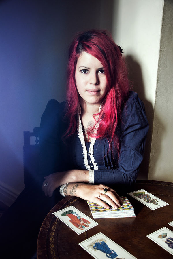 Photograph of the French-born tarot reader and scholar Laetitia Barbier sitting at a table—where a few cards from a tarot deck rest.