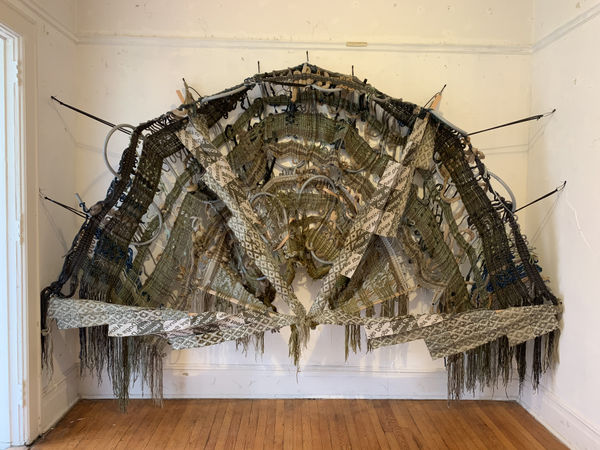 “No Dogs Allowed”, 95" x 127" x 20", loomed fabric in double-cloth, overshot, and warp-faced plain weave. Nonmetallic conduit and other plastics; wool, silk, cotton, linen, and other yarns; oak trim; leashes. 2021, image courtesy of the artist, copyright Kira Dominguez Hultgren