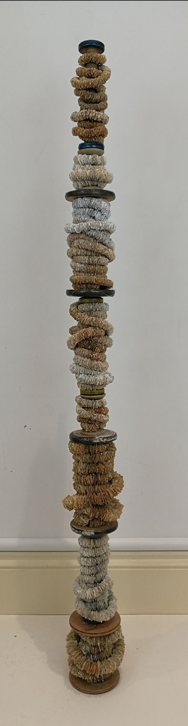115cm high stack of wooden bobbins. 1cm squares of naturally aged book paper threaded onto nylon are wrapped around each one.