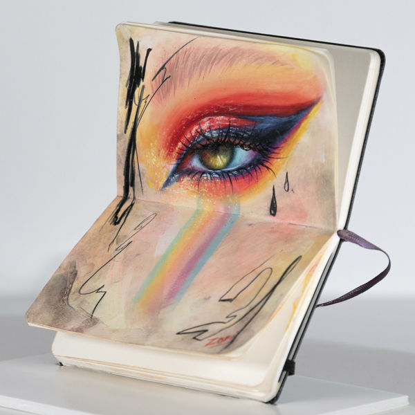 drawing of an eye with colorful eye makeup done on the pages of a moleskin notebook