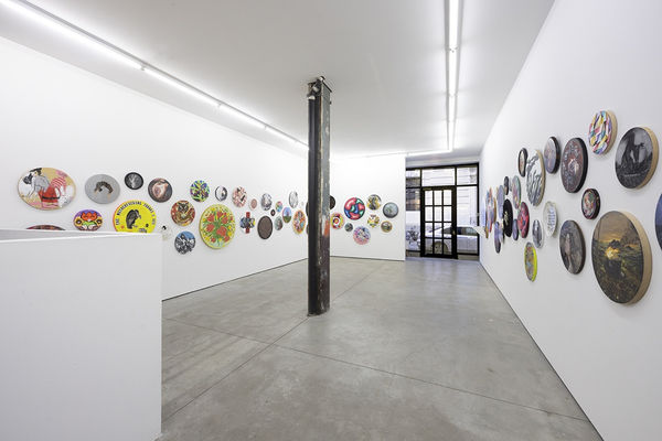 installation image of many round format artworks displayed on a white wall